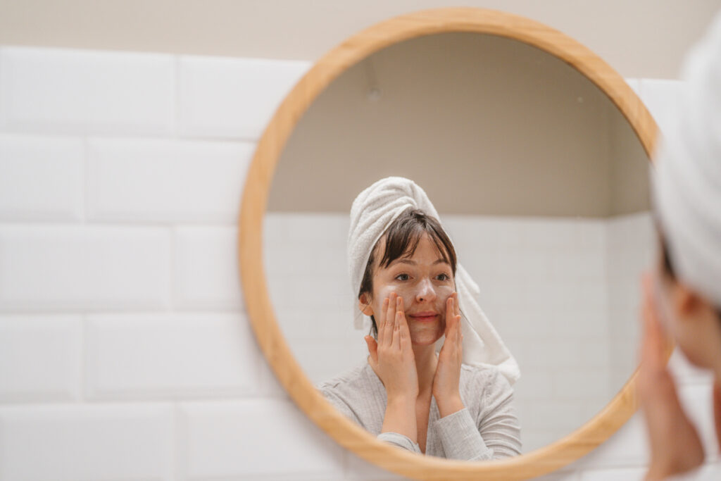 Photo of woman applying cream on her face while looking in the mirror